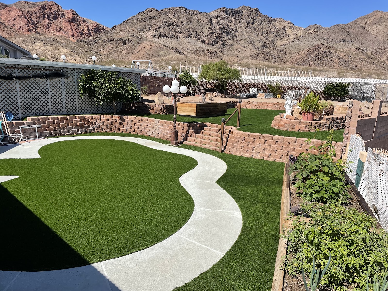 Artificial turf yard with curved concrete path, stone retaining walls and mountain backdrop