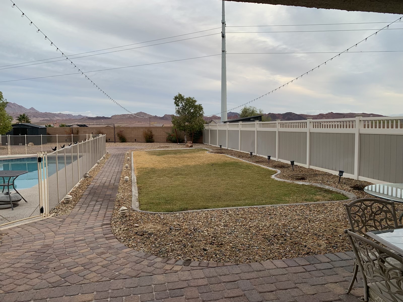Backyard with sod lawn, gravel borders, paver walkway and pool under overcast sky