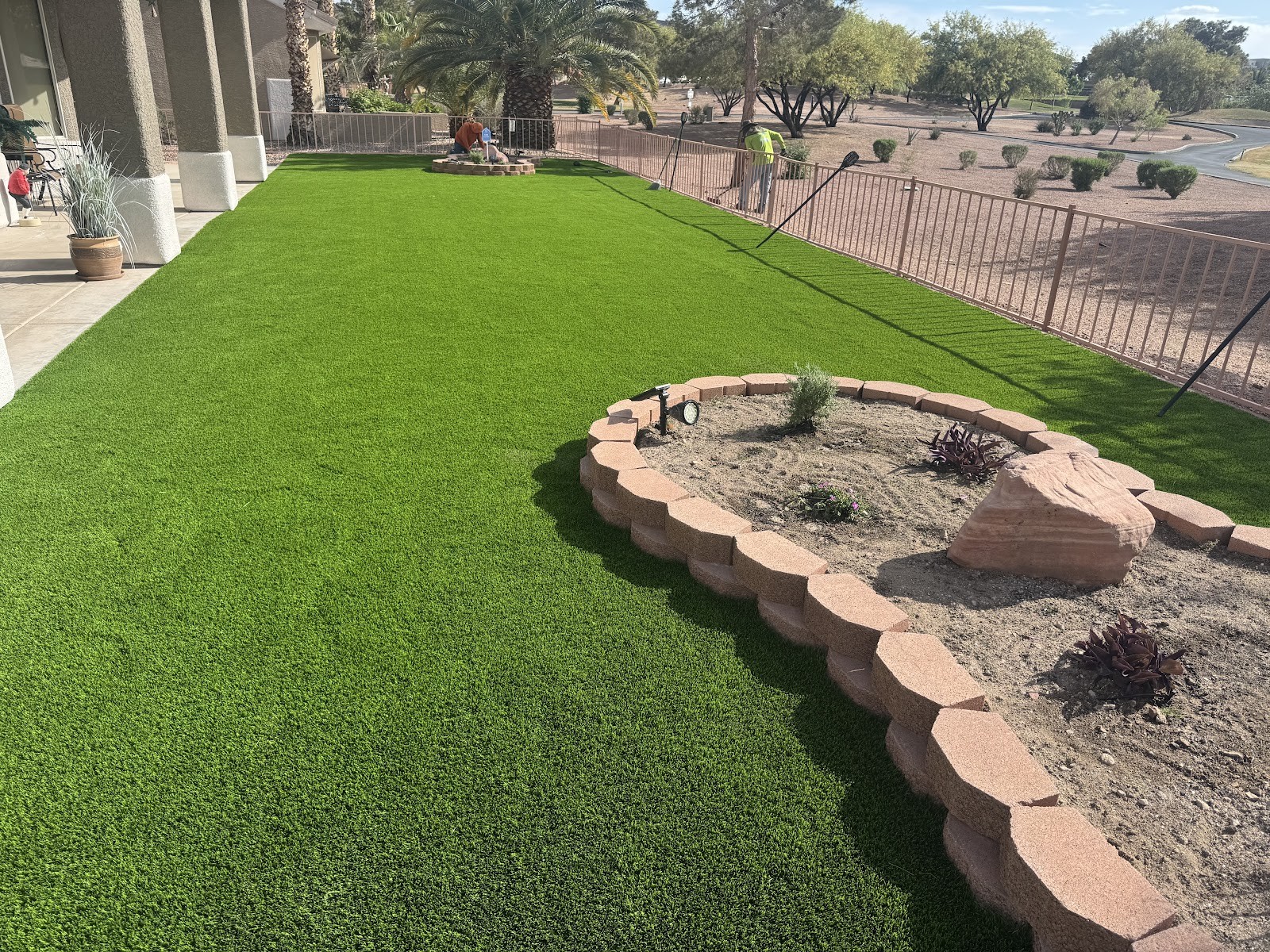 Lush artificial turf lawn with stacked-stone raised planter bed and desert plants
